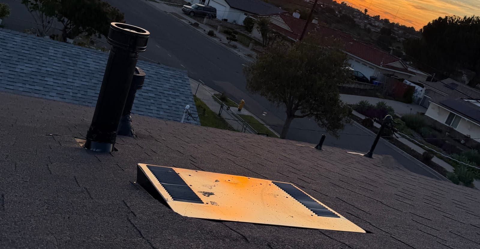 Close view of roof vents and an attic fan on new shingles at sunset