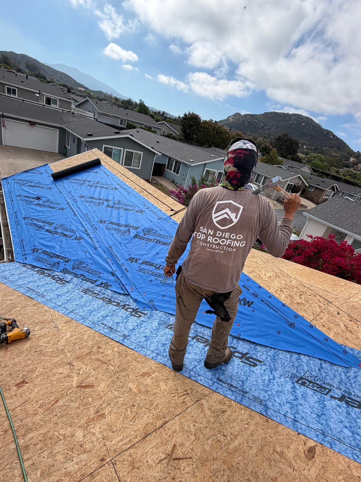 Crew member in a San Diego Top Roofing shirt rolling out synthetic underlayment over new decking
