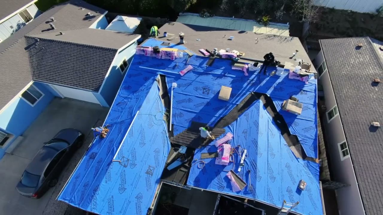 Drone view of a re-roof dried in with fresh underlayment, crew working the ridge
