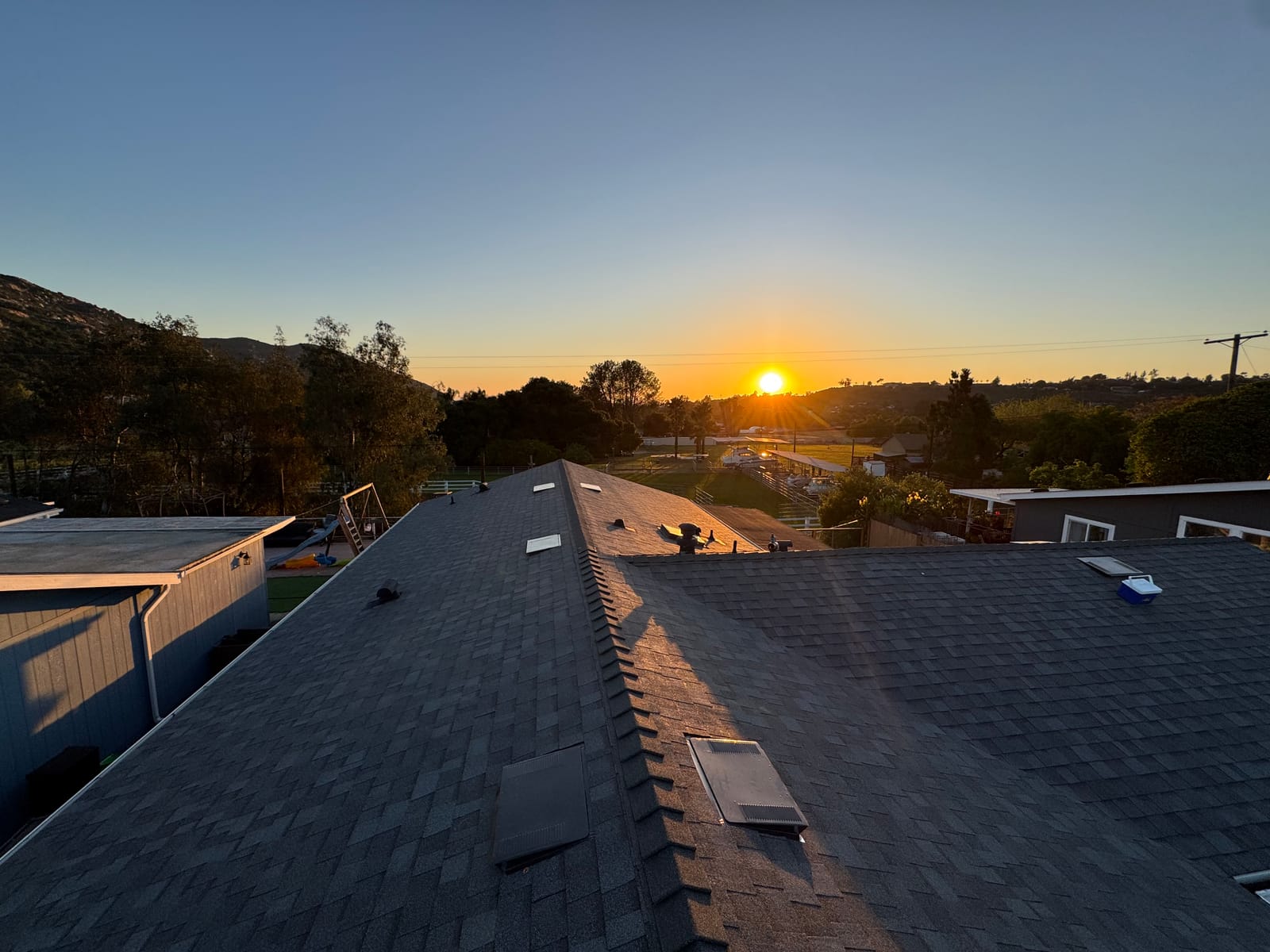 Completed architectural shingle roof at sunset, clean ridge lines and new vents against the hills